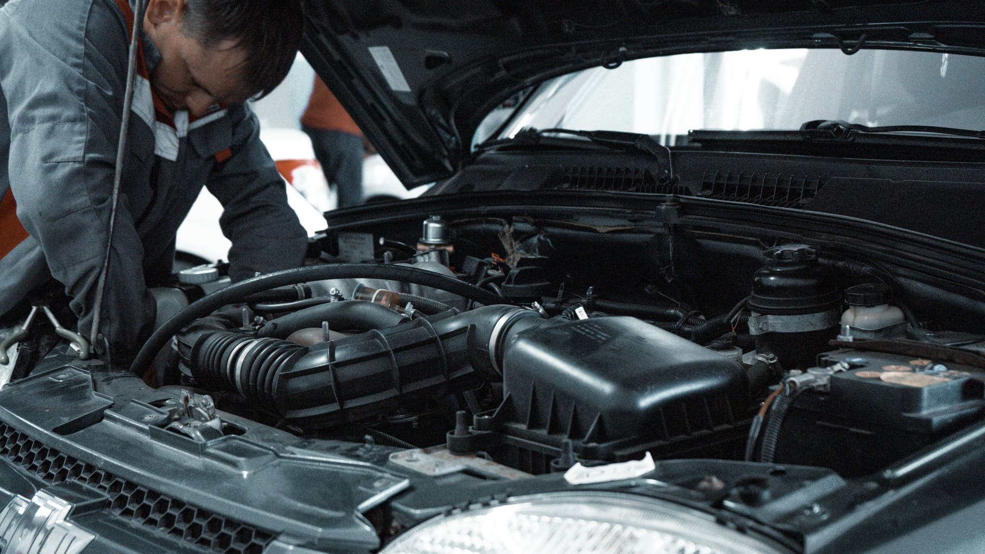 A technician leaning into the engine bay of a vehicle in a workshop, the intake and air-box assembly in the foreground.